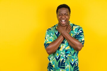 Young latin man wearing hawaiian shirt over yellow background shouting suffocate because painful...