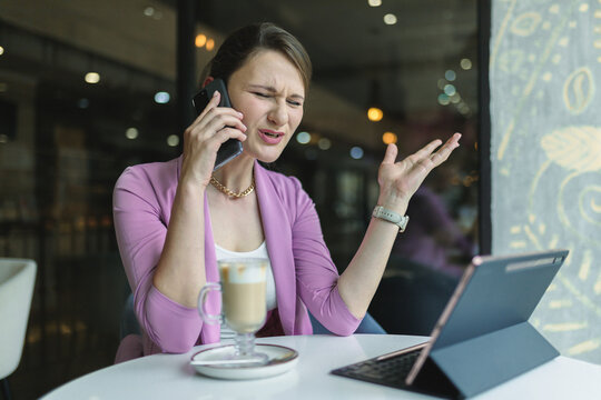 Upset Young Business Woman Emotionally Talking On The Phone In A Cafe.