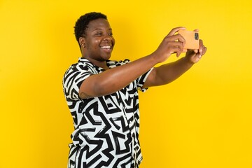  Young latin man wearing printed shirt over yellow background taking a selfie to post it on social...