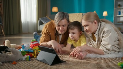 Young parents mother and father with their little kid spending time together watching tablet