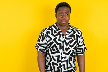 Portrait of dissatisfied  Young latin man wearing printed shirt over yellow background smirks face,...