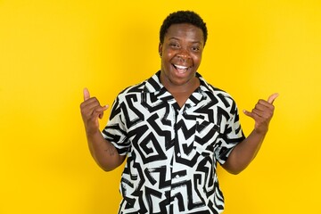  Young latin man wearing printed shirt over yellow background makes rock n roll sign looks self confident and cheerful enjoys cool music at party. Body language concept.