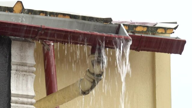 Rain streams flow down from clogged drain pipe along house wall 
