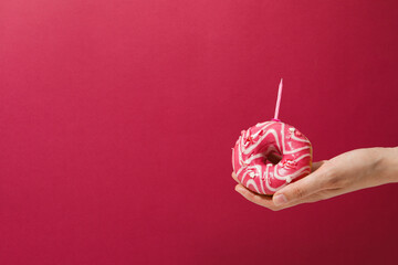 Pink glazed donut with candle in female hand on pink background, space for text