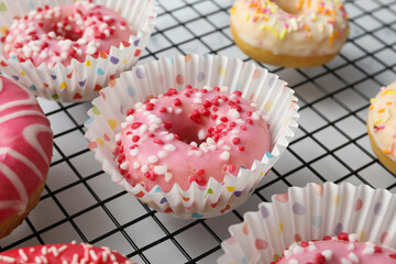 Donuts in paper cupcake cups on grid on white background, close up