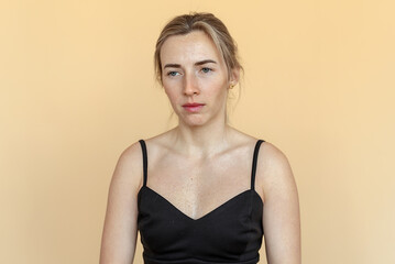Fototapeta premium Portrait of the thoughtful upset woman standing over beige background, lost in thoughts. Pensive unhappy girl feeling lonely and depressed, thinking about relationship or personal problems