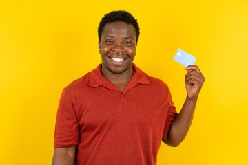 Photo of happy cheerful smiling positive Young latin man wearing red t-shirt over yellow background recommend credit card