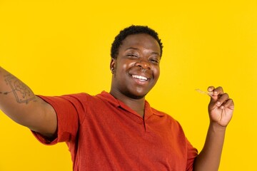 Young latin man wearing red t-shirt over yellow background make selfie holding an invisible braces aligner, recommending this new treatment. Dental healthcare concept. - obrazy, fototapety, plakaty