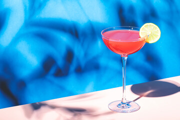 Siesta alcoholic cocktail drink with silver tequila, grapefruit and lime juice, syrup and italian red bitter liqueur, summer blue bright background, hard light and shadows