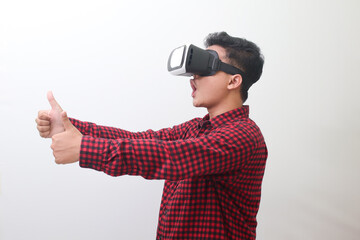 Portrait of Asian man in red plaid shirt using Virtual Reality (VR) glasses and showing thumb up hand gesture. Isolated image with copy space on white background.