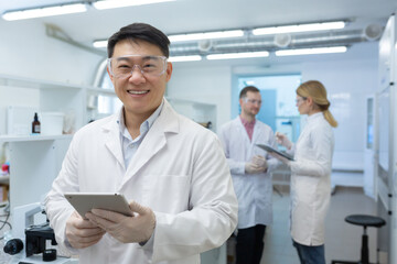 Portrait of an Asian laboratory technician scientist inside a laboratory, the man is looking at the camera and smiling, the scientist is working with colleaguesmanufacturing biological supplements.