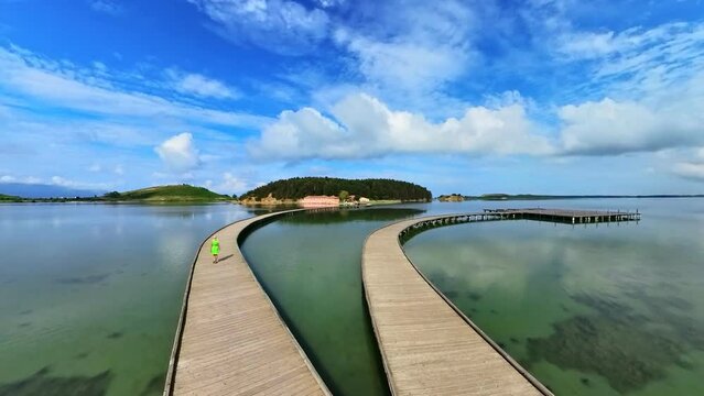 A woman stands on a pedestrian bridge on Zvernec Island, Albania. From a drone's view, she appears as a solitary figure amidst the idyllic landscape of Narta Lagoon.