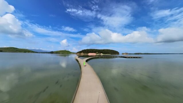 HYPER-LAPSE: drone view of woman tourist walking on pedestrian bridge to site on Zvernec Island in Narta Lagoon. Location of the Zvernec St. Mary Monastery near Vlora city on southwestern Albania.