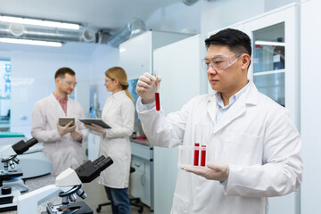 Serious asian scientist inside laboratory researching blood in test tubes, man in medical white coat.