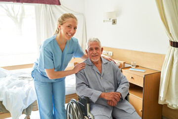 Smiling nurse with elderly man in wheelchair at rehab center - obrazy, fototapety, plakaty