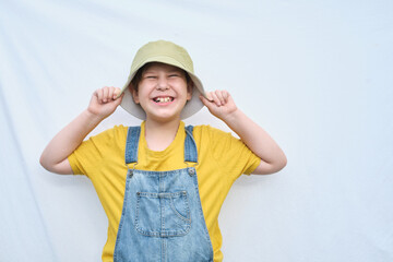 smiling boy dressed in a denim jumpsuit with a yellow shirt, ready to explore the world with his fashionable hat on, his crooked teeth adding charm to his joyful expression