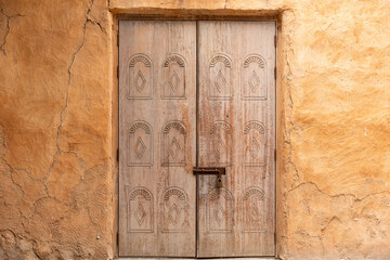 Ancient arabic wooden front door with oriental pattern. Door surrounded by a clay wall. Entrance of the house.