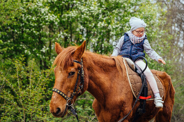 Little girl riding on a horseback. The girl is sitting on a horse . A child on a day walk on the ranch.