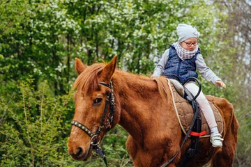 Foto op Canvas Little girl riding on a horseback. The girl is sitting on a horse . A child on a day walk on the ranch. © Iryna