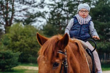 Little girl riding on a horseback. The girl is sitting on a horse . A child on a day walk on the...