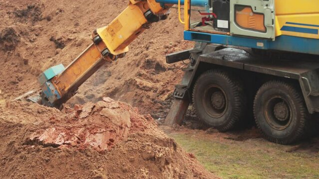 An excavator with a retractable boom and a swivel bucket is digging a hole to replace the heating main. Copy space for text