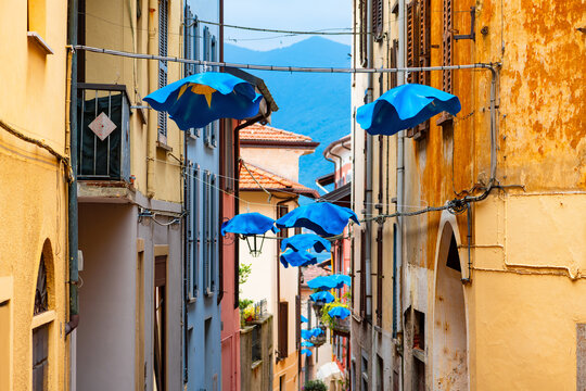 Narrow street in the old town of Luino at lake &ldquo;Lago Maggiore&ldquo; in Italy. Colorful facades, balconys and shops. Popular tourist destination and famous market place on a summer day. Idyllic alley lane.