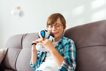 A cute child boy sitting indoors at home, playing with robotic dog. Best friend and loneliness