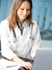 Portrait of cheerful female doctor working with laptop at office