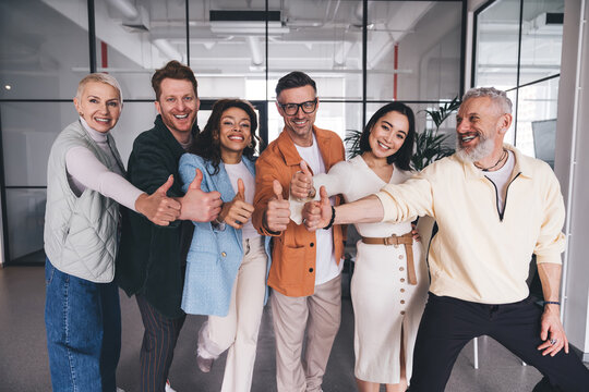 Cheerful multiethnic colleagues joining hands with thumbs up gesture in circle