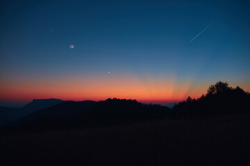 Silhouette of a countryside with Milky Way stars, shooting star, planets and crescent Moon.