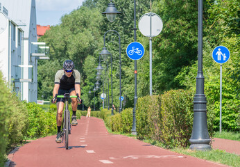 Boy with helmet cycling on the bike road with blue road sign or signal of bicycle lane among green...