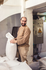 Smiling worker holds a sack in a factory