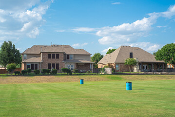 Fototapeta na wymiar New development two story houses near rolling grassy lawn of suburban park in Flower Mound, Texas, America