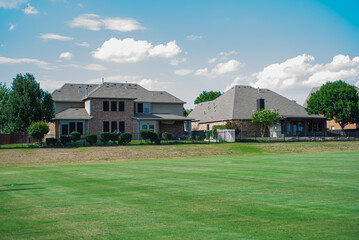 Fototapeta na wymiar Large grassy and rolling lawn of suburban park next to upscale residential neighborhood row of two-story houses in Flower Mound, Texas, USA