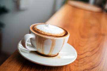 Spilled coffee with milk in a white cup or cappuccino is overflowing from the coffee cup on wooden bar