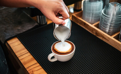 Fototapeta na wymiar Barista hand pouring milk into coffee making a cappuccino. Professional barista preparing coffee on the counter.