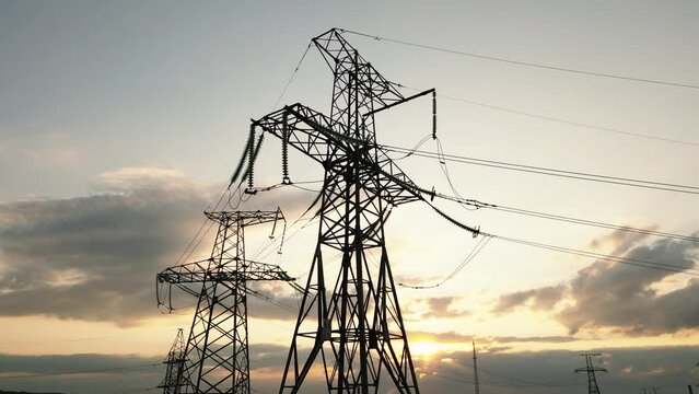 Transmission tower supporting an overhead high voltage power line - silhouette at sunset. The pylon carries wires that transport electric power from generating stations to electrical substations.
