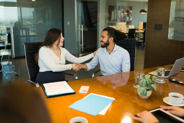 Smiling pregnant businesswoman shaking hands with coworker in office conference room