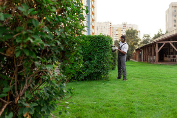 Fototapeta na wymiar garden worker in uniform cuts bushes, african american man in goggles and headphones works in the garden