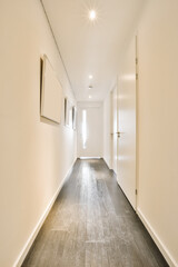 an empty white room with wood flooring and light fixtures on the wall in the hallway is lit by recessed lights