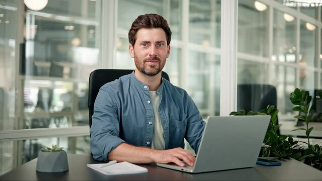 Focused handsome businessman professional financial advisor, executive leader, manager, female lawyer or man entrepreneur standing in office working on laptop rasing head looking friendly to camera.