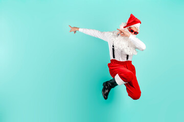 young guy dressed as santa claus in shirt with suspenders jumps and points to the side