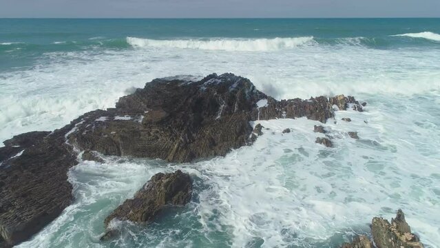 Slow backward drone flight over rocky coast with waves crashing on the rocks, Atlantic coast of west Portugal
