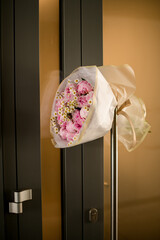 Entrance door with bouquet of peonies and camomile in white wrapping paper. different seasonal flowers.