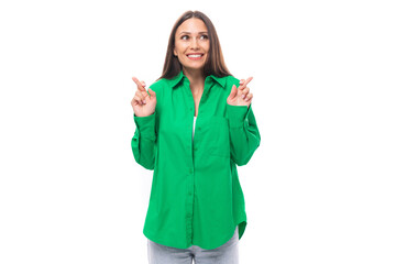 young caucasian brunette lady with make-up dressed in an elegant green shirt points with her hands towards the wall with empty space