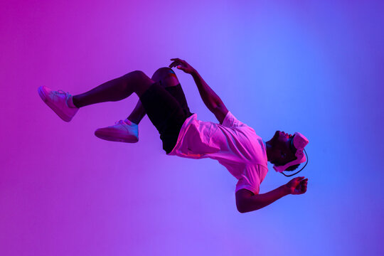 african american male gamer in virtual reality glasses flies in the air and falls in neon lighting, guy plays with vr