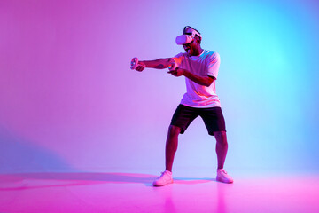 Fototapeta na wymiar african american man in virtual reality glasses aiming and shooting in neon lighting, guy gamer playing