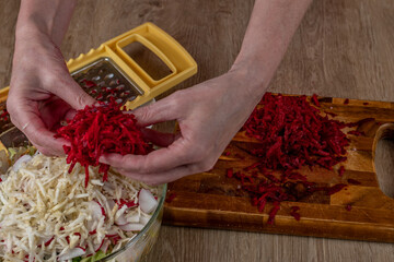 Female prepares a fresh vegetable salad. Close-up grates red beets on an iron grater for making fresh vegetable salad. Delicious vegetable salad is good for health. Concept of a healthy lifestyle