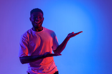 african american man shows his hands to the side in neon lighting, guy smiles and advertises copy space