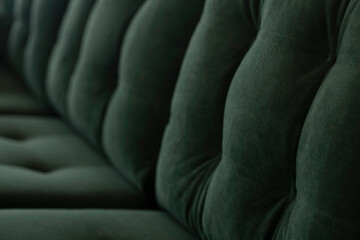 Soft vintage sofa in green velor with a quilted seat and a back of stitched cushions. Part of stylish furniture covered with plush fabric in emerald color close-up.